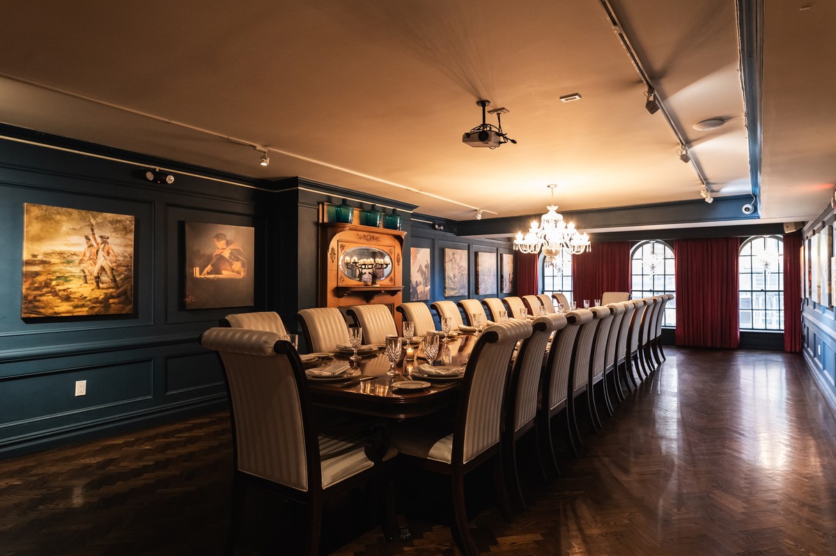 Dining room with a long table set for a meal, surrounded by classic paintings on dark blue walls.