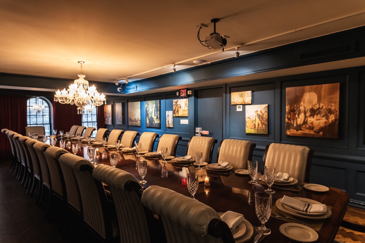 Dining room with a long table set for a meal, surrounded by classical paintings.