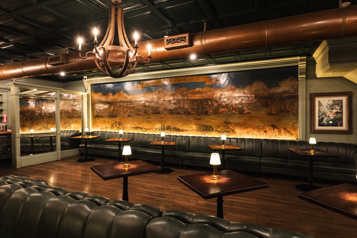 Elegant vintage-style bar with leather banquettes, small wooden tables, lit lamps.